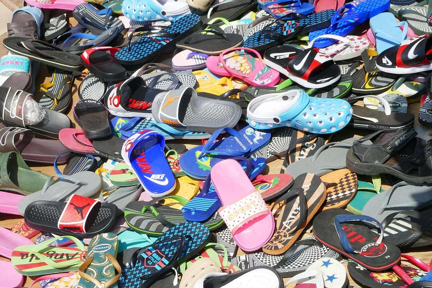 A colourful, messy pile of worn rubber sandals strewn across the ground.